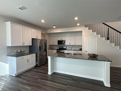 Kitchen with dark stone counters, appliances with stainless steel finishes, white cabinetry, tasteful backsplash, and dark wood-type flooring