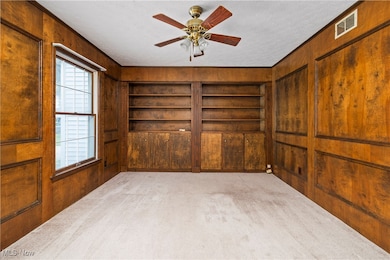 Spare room with wooden walls, carpet floors, a textured ceiling, built in shelves, and ceiling fan