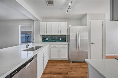 Kitchen featuring light wood finished floors, stainless steel appliances, track lighting, tasteful backsplash, and light stone countertops