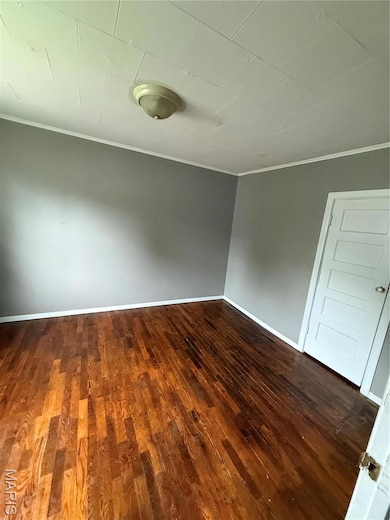 Spare room featuring ornamental molding and dark wood finished floors
