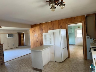 Kitchen with wood walls, a peninsula, freestanding refrigerator, light countertops, and a wall mounted AC