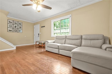 Living area featuring ornamental molding, light wood-style flooring, a ceiling fan, and baseboards
