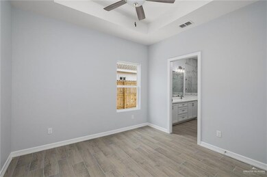 Unfurnished bedroom featuring a tray ceiling, wood tiled floors, ensuite bath, and a ceiling fan
