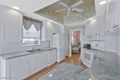Kitchen featuring white appliances, white cabinetry, light wood-style floors, a tray ceiling, and a sink