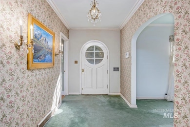 Carpeted entryway with crown molding, wallpapered walls, a chandelier, and arched walkways