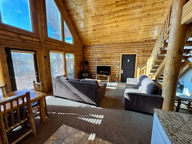 Carpeted living area with high vaulted ceiling, log walls, wooden ceiling, and a wood stove