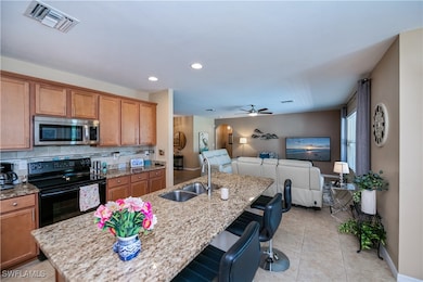 Kitchen featuring stainless steel microwave, black electric range oven, open floor plan, a kitchen bar, and ceiling fan