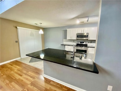 Kitchen with white cabinetry, decorative light fixtures, light wood-style flooring, stainless steel appliances, and backsplash