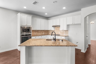 Kitchen with light stone countertops, white cabinetry, arched walkways, tasteful backsplash, and dark wood-style floors