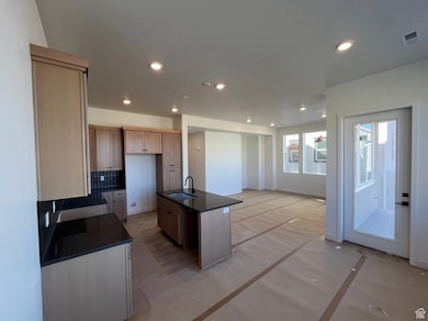 Kitchen featuring a center island with sink, recessed lighting, tasteful backsplash, dark stone counters, and concrete floors