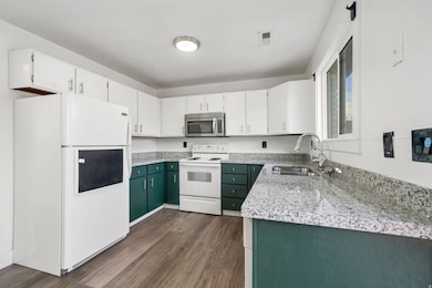Kitchen featuring white appliances, white cabinetry, light stone counters, dark wood finished floors, and green cabinets