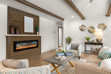 Living room featuring beamed ceiling, wood-type flooring, and ceiling fan