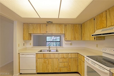 Kitchen with white appliances, light countertops, exhaust hood, light tile patterned flooring, and light brown cabinets