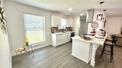 Kitchen featuring a breakfast bar, white cabinetry, backsplash, island range hood, and light countertops
