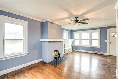 Unfurnished living room featuring crown molding, hardwood floors, a decorative fireplace, and ceiling fan.  Most windows have been replaced.