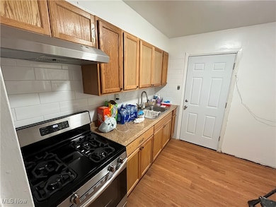 Kitchen with stainless steel gas range, tasteful backsplash, light countertops, under cabinet range hood, and brown cabinets