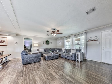 Living room featuring a textured ceiling, wood finished floors, ceiling fan, and ornamental molding