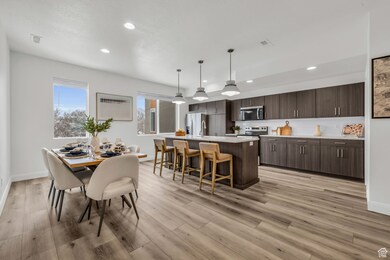 Interior space with pendant lighting, light countertops, stainless steel microwave, dark brown cabinetry, and an island with sink