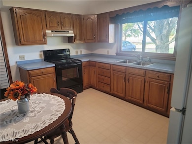 Kitchen featuring black / electric stove, brown cabinetry, freestanding refrigerator, and light floors