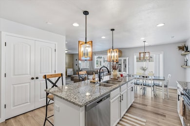 Kitchen featuring light stone countertops, a breakfast bar area, stainless steel dishwasher, light wood-style flooring, and white cabinetry