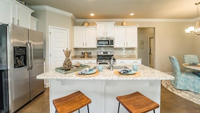 Kitchen featuring stainless steel appliances, white cabinetry, ornamental molding, a chandelier, and backsplash