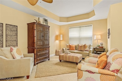 Living area with light tile patterned floors, a ceiling fan, and a raised ceiling