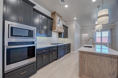 Kitchen with appliances with stainless steel finishes, light countertops, light wood-type flooring, an island with sink, and crown molding