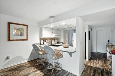 Kitchen with dark wood finished floors, decorative backsplash, white cabinetry, recessed lighting, and a kitchen breakfast bar