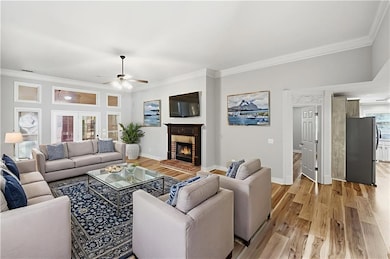 Living area featuring crown molding, light wood-style floors, a fireplace, and a ceiling fan