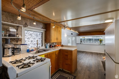 Kitchen featuring brown cabinetry, freestanding refrigerator, a peninsula, light countertops, and white range with gas cooktop