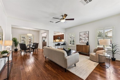 Living room featuring dark wood-type flooring, ornamental molding, and ceiling fan