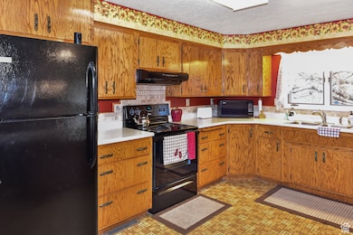 Kitchen featuring black appliances, brown cabinetry, light countertops, ventilation hood, and a textured ceiling