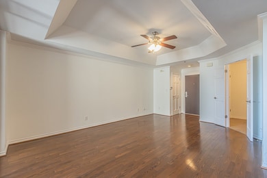 Empty room with a ceiling fan, a raised ceiling, wood finished floors, and ornamental molding