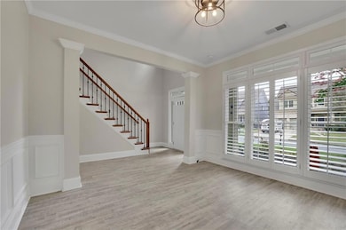 Entryway featuring crown molding, stairs, wainscoting, light wood-type flooring, and a decorative wall