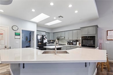 Kitchen featuring dark wood-style floors, backsplash, gray cabinets, recessed lighting, and black appliances