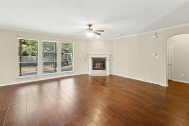 Unfurnished living room featuring ceiling fan, arched walkways, dark wood-type flooring, crown molding, and baseboards