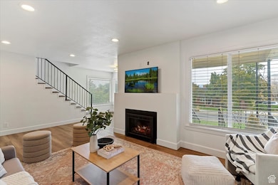 Living room with a lit fireplace, wood finished floors, recessed lighting, and stairway