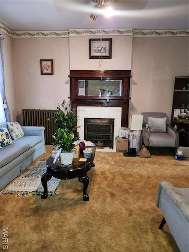 Living room featuring a fireplace, radiator, carpet, and wallpapered walls