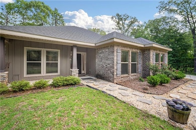 View of front of property with board and batten siding, roof with shingles, a front lawn, and brick siding