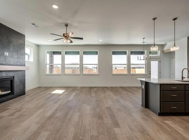Kitchen with a sink, light countertops, ceiling fan, light wood-type flooring, and a tile fireplace