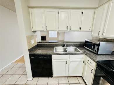 Kitchen with black appliances, white cabinetry, dark countertops, and light tile patterned flooring