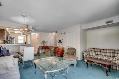 Carpeted living area featuring a chandelier and a textured ceiling