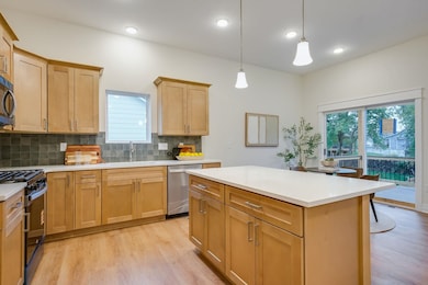 Kitchen with light wood finished floors, tasteful backsplash, appliances with stainless steel finishes, hanging light fixtures, and a center island