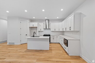 Kitchen featuring white cabinetry, a kitchen island with sink, backsplash, recessed lighting, and light wood-type flooring