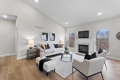 Living room featuring a glass covered fireplace, recessed lighting, light wood finished floors, and high vaulted ceiling