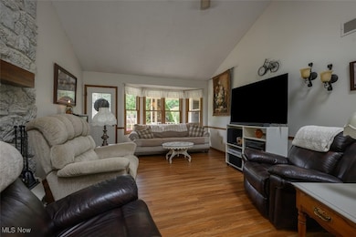 Living room with large bay window, stonewall fireplace, vaulted ceiling and ceiling fan