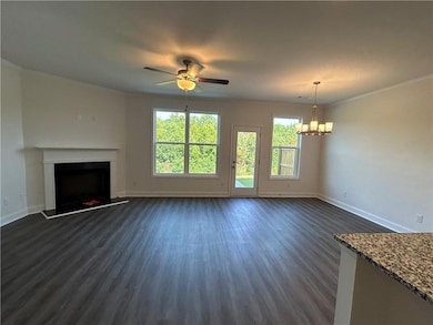 Unfurnished living room featuring dark wood-style floors, a fireplace with raised hearth, ceiling fan, and a chandelier