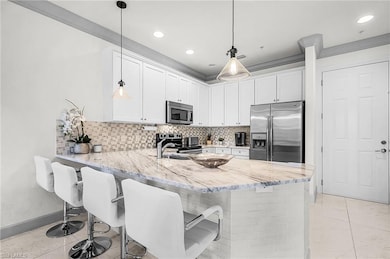 Kitchen with stainless steel appliances, a breakfast bar area, a peninsula, white cabinets, and decorative backsplash