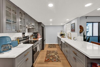 Kitchen with gray cabinetry, black appliances, a peninsula, decorative backsplash, and light wood-style flooring