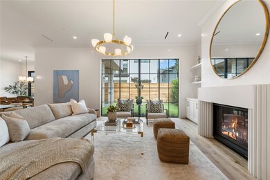 The luxe living room, featuring 11-foot ceilings, showcases a gas-log fireplace flanked with custom cast stone surround and mantle.  Sprawling custom windows flood the space with natural light—which bounces off the Venetian plaster walls.